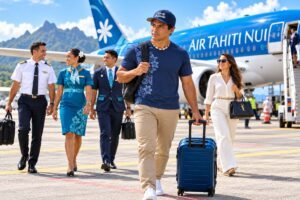 Voyager avec la goutte : homme avec valise cabine bleue sur le tarmac, devant un avion Air Tahiti Nui.
